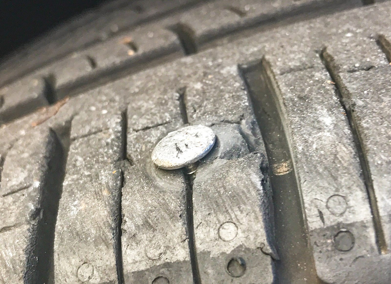 Close-up of a nail head embedded in the tread of a car tire