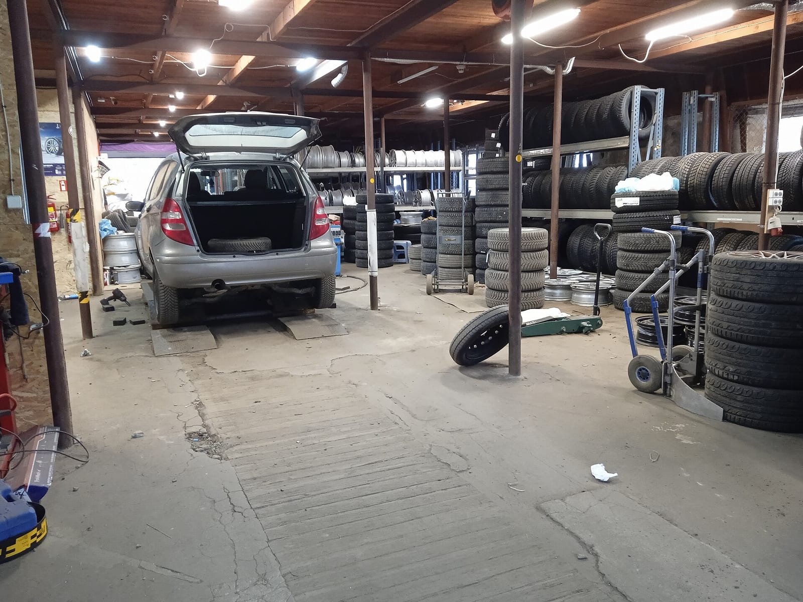 Tire shop interior with a hatchback in a service bay, tires stacked on shelving and a loose wheel on the floor