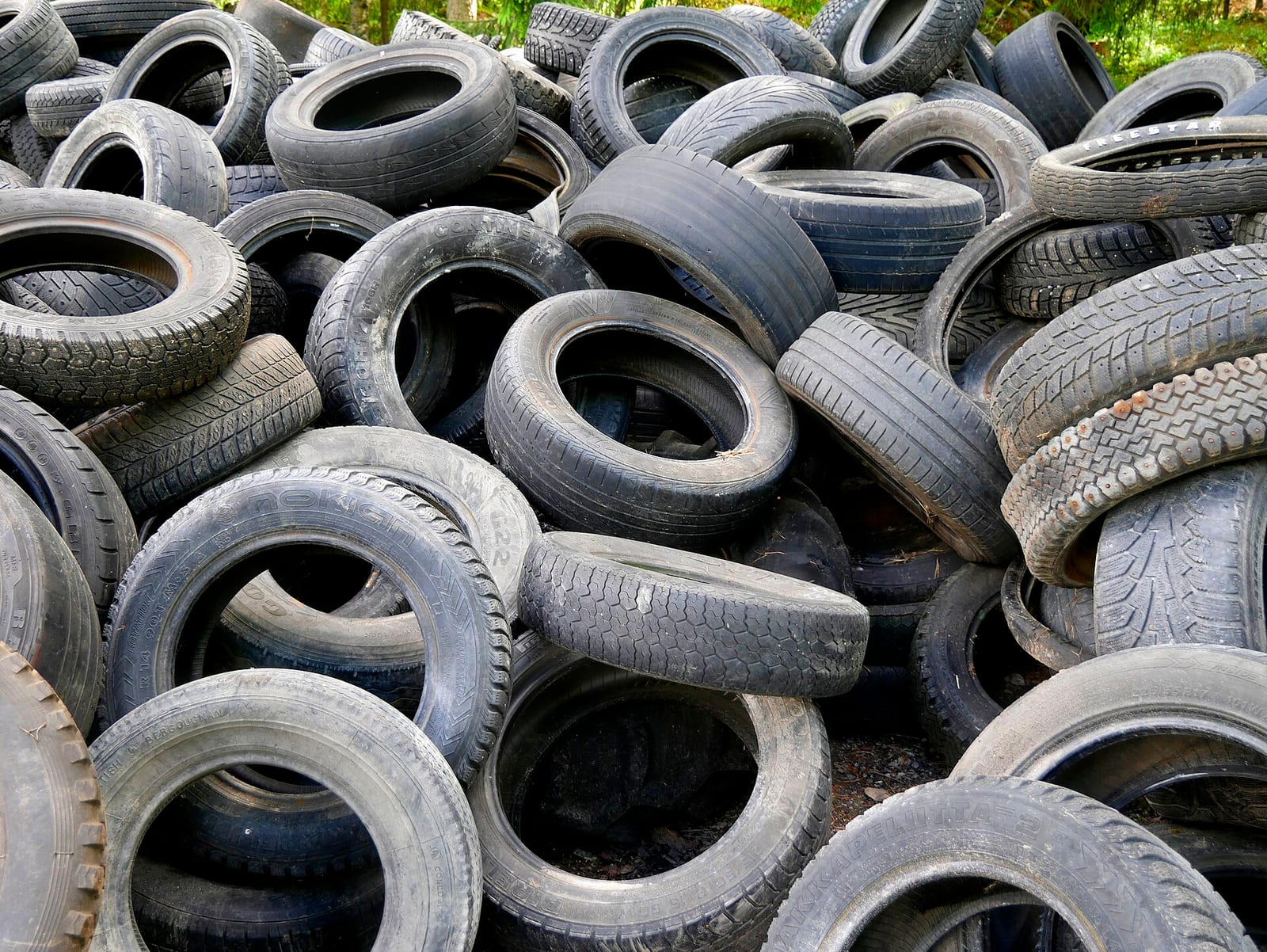 A large outdoor pile of used car tires with mixed tread patterns, some worn close to smooth