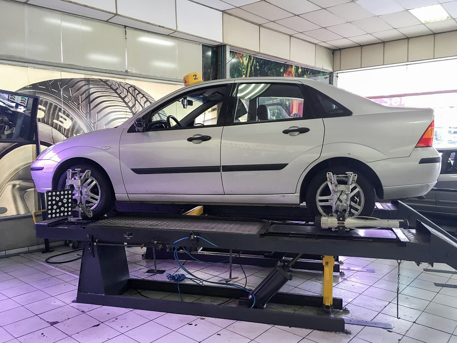 Silver sedan on a raised alignment lift with measuring clamps fitted to its front and rear wheels